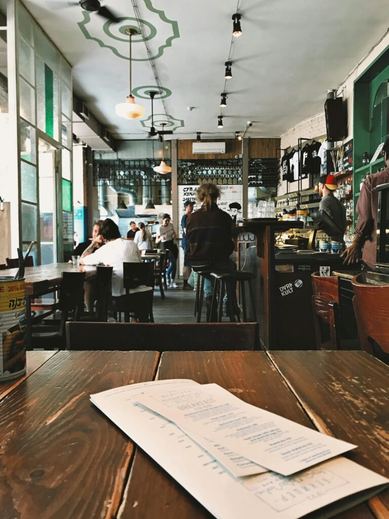 Cozy coffee shop interior with people dining and a rustic wooden table in focus.